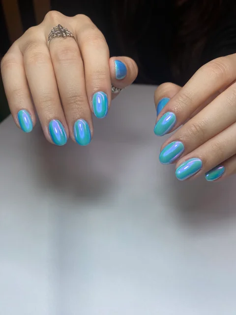 Manicura azul con reflejos iridiscentes verdes y violetas.