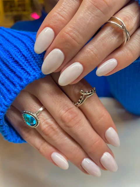 Uñas almendradas de acabado blanco lechoso junto a un jersey azul.