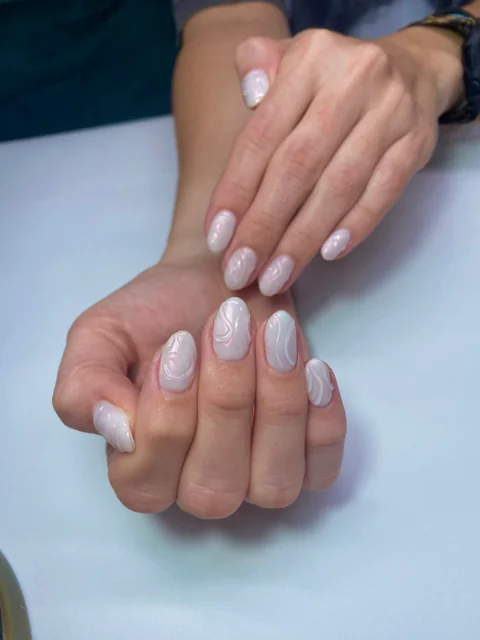Manicura nacarada con líneas blancas en relieve sobre uñas almendradas.